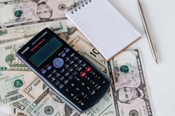 calculator and notepad placed over dollar bills